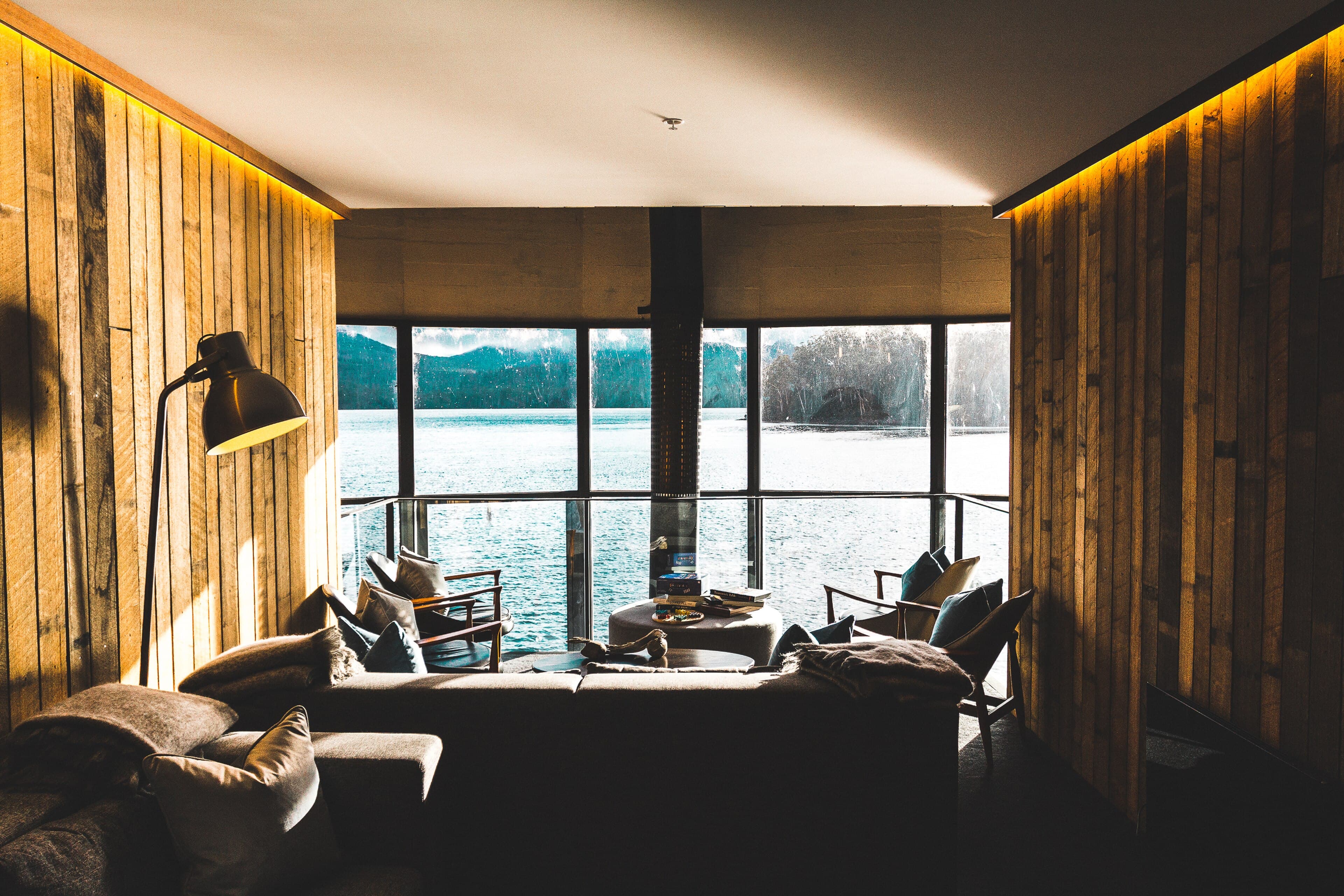 A timber-lined sitting room with low chairs facing a wall of windows over a lake